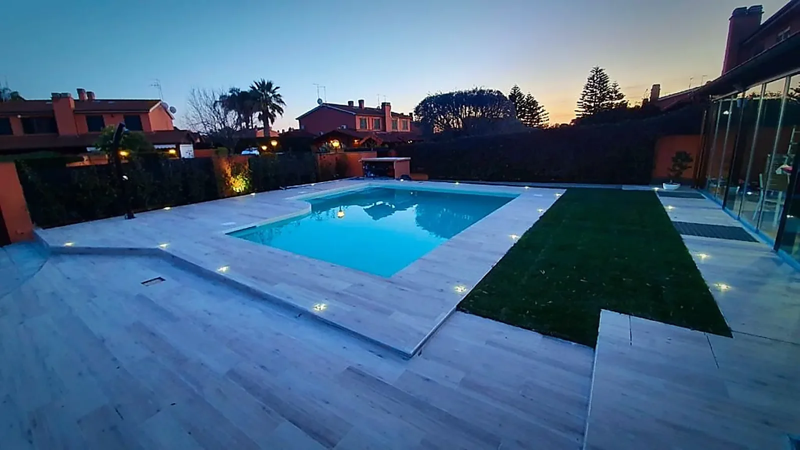 Piscina con bordo in pietra e prato al tramonto